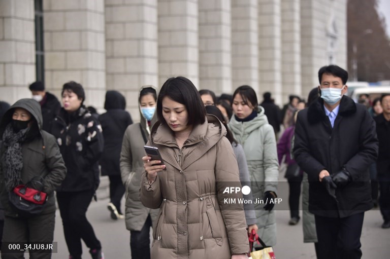 Piétons qui sortent de la gare de Pyongyang, tandis qu'une femme utilise son téléphone portable