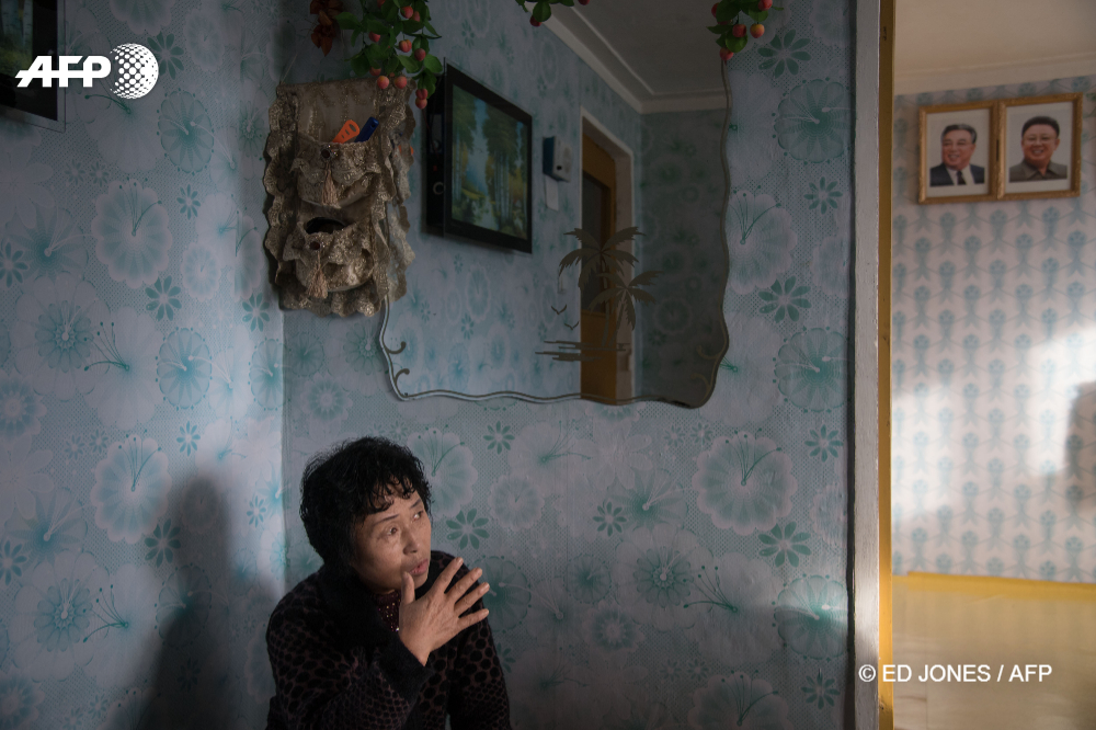 Une femme est assise dans sa maison devant les portraits des deux leaders nord-coréens