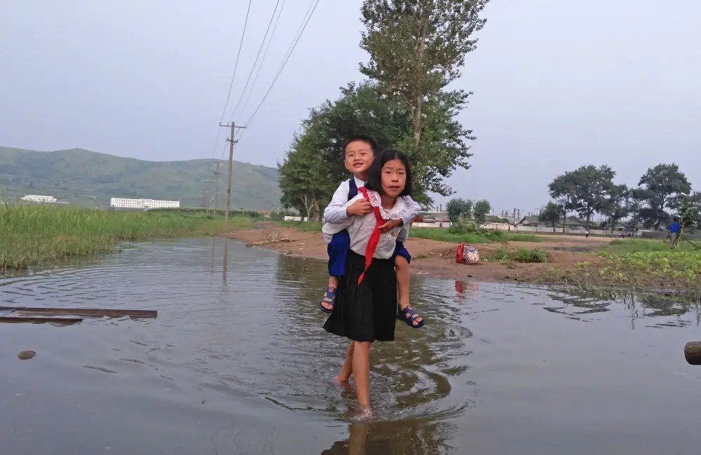 Deux enfants vont à l'école, sur une route inondée
