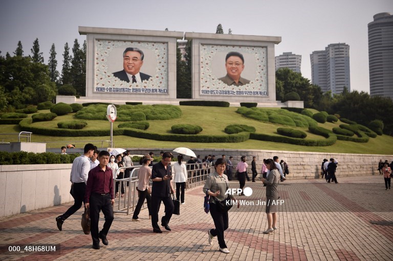 Des nord-coréens marchent dans la rue, devant les portraits gigantesques des deux leaders Kim Il Sung et Kim Jong Il